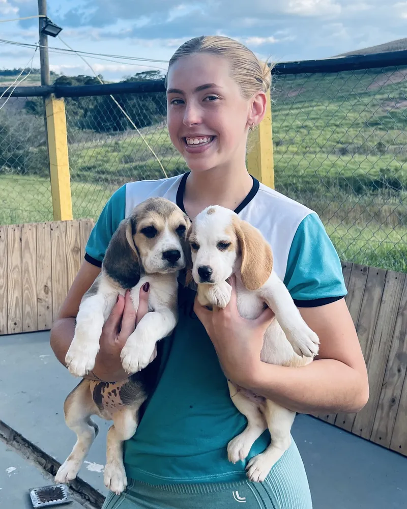Moça sorrindo com um filhote de Beagle em cada braço